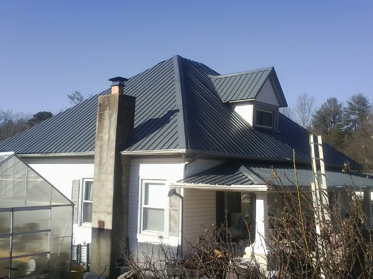 Dark blue standing seam metal roof on a white farmhouse with dormer — Slate & Tile Roof Repair by Roofing Brothers in Alvord