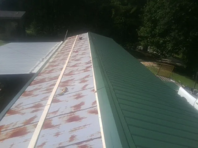Old rusted panels beside newly installed green metal roofing — Wind Damage Roof Repair by Roofing Brothers in Alvord