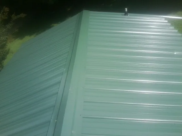 New green metal panels meeting at the ridge of a roof — Flat Roof Repair work by our crew in Alvord