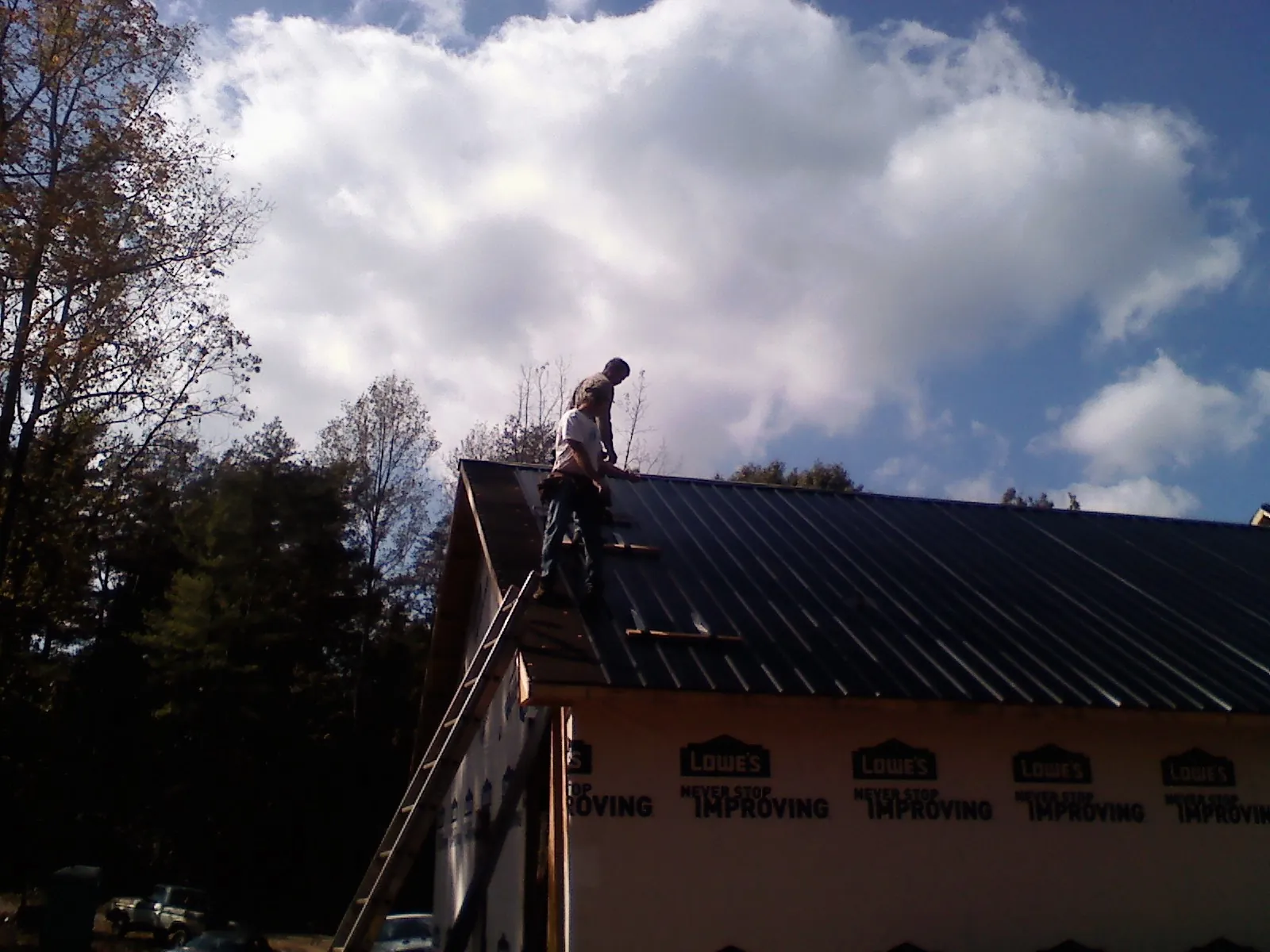Roofer fastening dark metal panels high against a cloudy sky, from a Roof Inspection job in Alvord