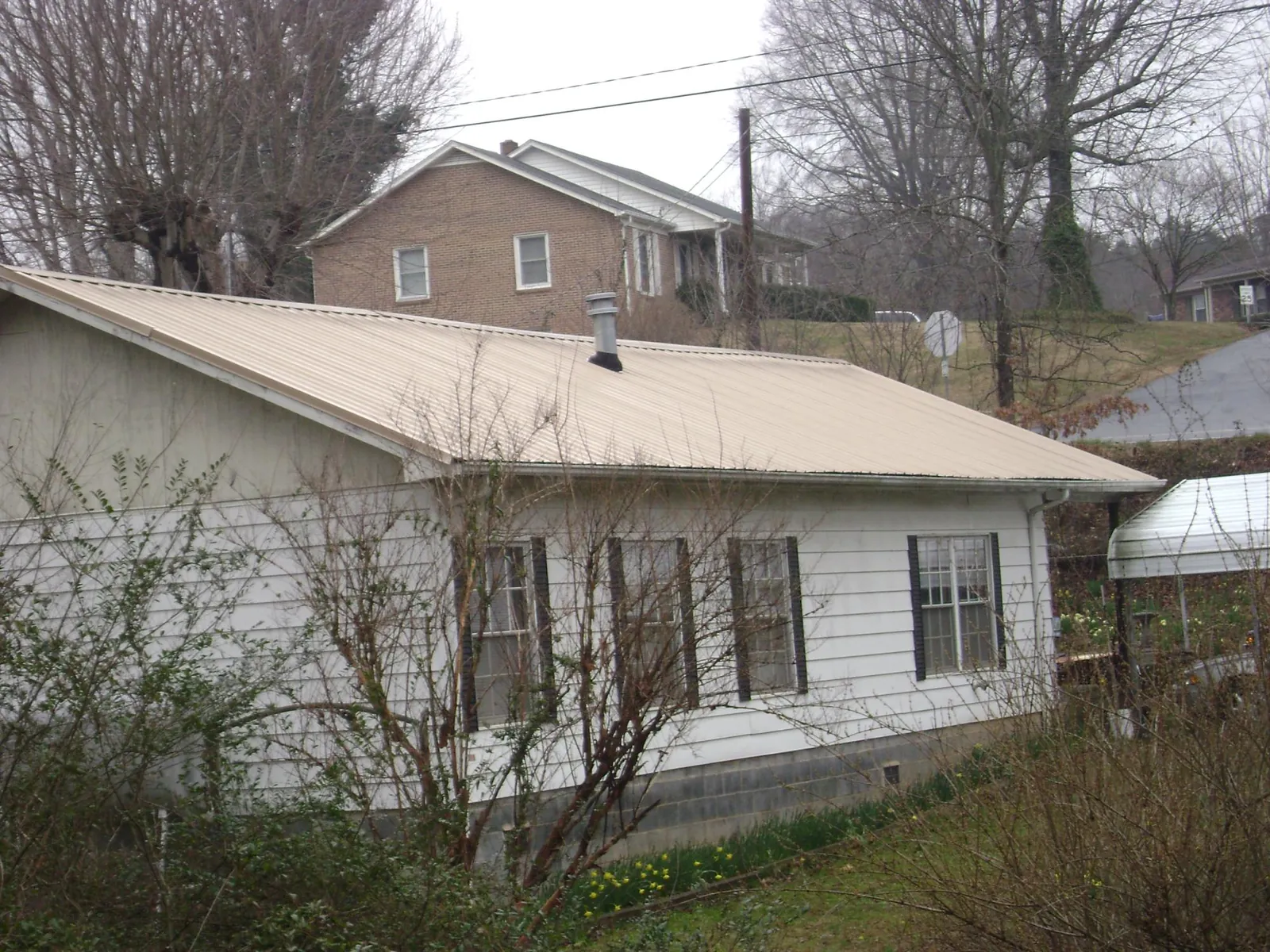 Tan metal roof on a white sided house set into a hillside — Commercial Roofing by Roofing Brothers in Alvord