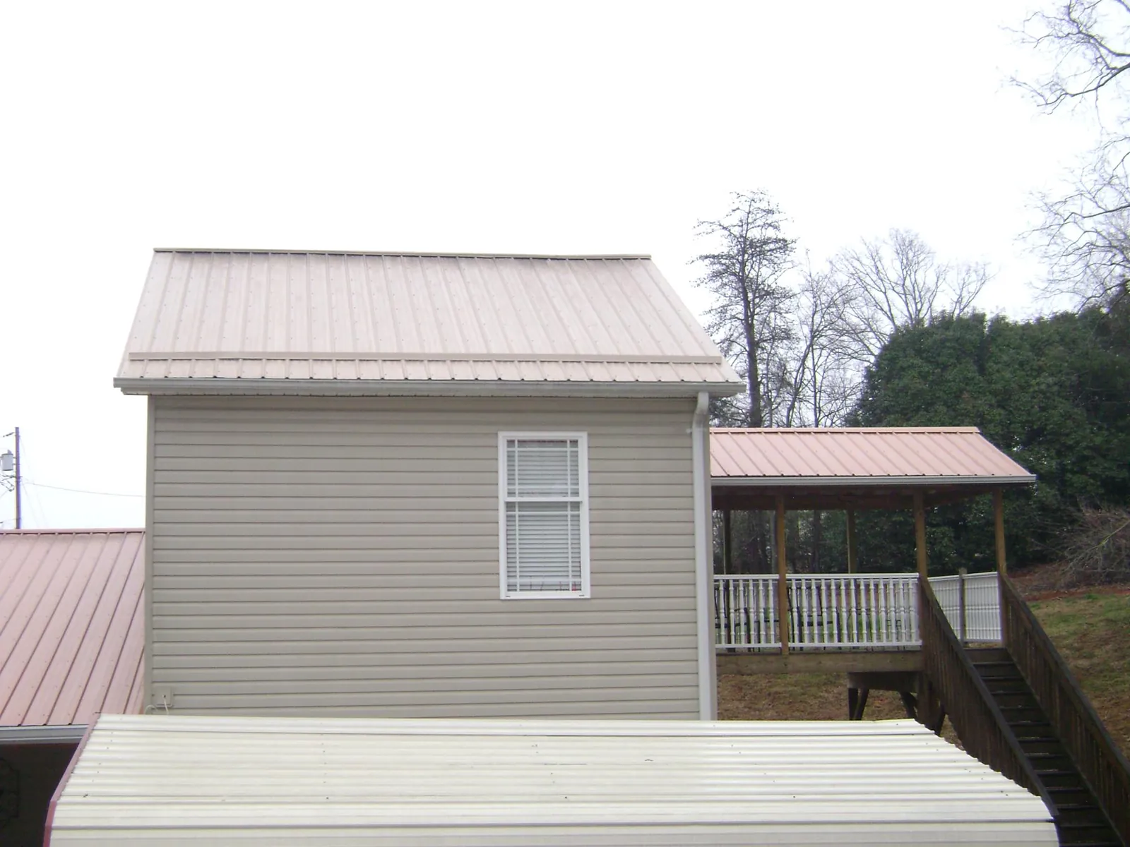 Tan metal roofs on a two story addition and attached porch, from a Roof Replacement job in Alvord